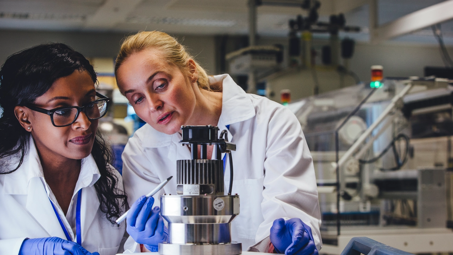 Two female lab workers in white coats and gloves Two female lab workers in white coats and gloves
